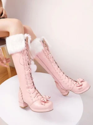 Pink knee-high Lolita chunky heel platform boots with furry collar and lace-up front featuring bow ornament, worn by model in studio setting