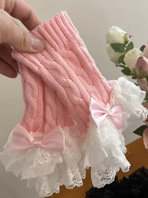 Pink sweet lolita knitted wrist and leg cuffs with white lace ruffles pink satin bows cable knit texture close-up handheld perspective with artificial rose decoration