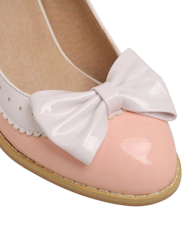 Close-up front top view of single pink lolita pump shoe with large white bow ornament scalloped white trim glossy toe cap on white background