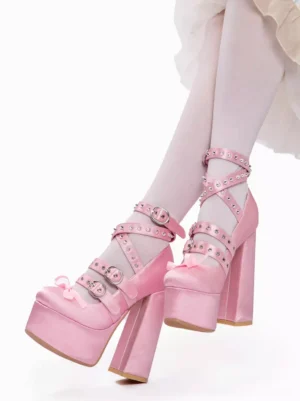 Pink satin lolita platform pumps side view with criss-cross riveted straps, chunky heel, and front bow accent paired with white thigh-high stockings and white frilly lolita skirt
