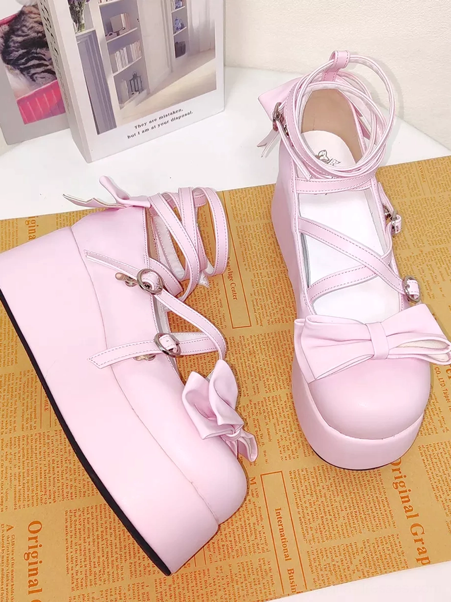 Pink Lolita platform pumps flat lay perspective with newspaper-style backdrop and decorative book showing side heel bow and light pink smooth PU leather finish