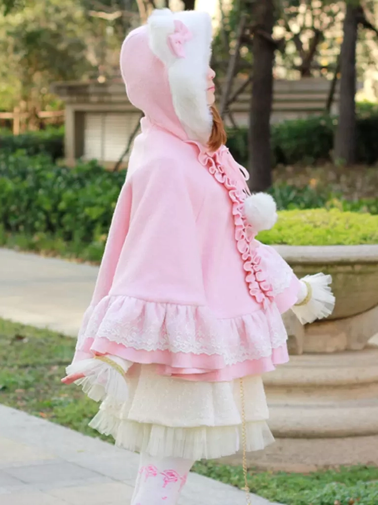 Pink sweet lolita poncho coat rear side view with cat ear hood up on model wearing coordinated outfit in garden, displaying back lace ruffle hem and cape silhouette
