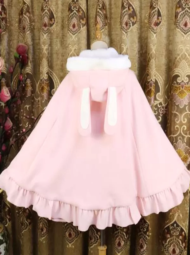 Pink Lolita poncho coat back view showing bunny ear hood design, ruffled hem, and solid pink fabric on vintage patterned curtain backdrop