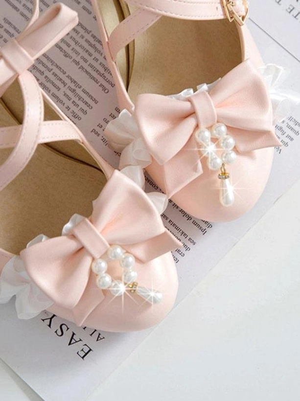 Pink lolita chunky heel pumps close-up overhead view showing detailed shoe interior, cross strap construction, pearl bow ornament embellishment, delicate ruffle trim, and soft pink polyurethane leather material