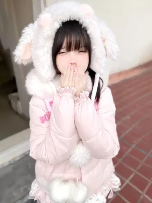Sweet lolita pink puffer coat medium shot detail of fluffy animal ear hood and pom pom trims hands gesture outdoor red brick backdrop