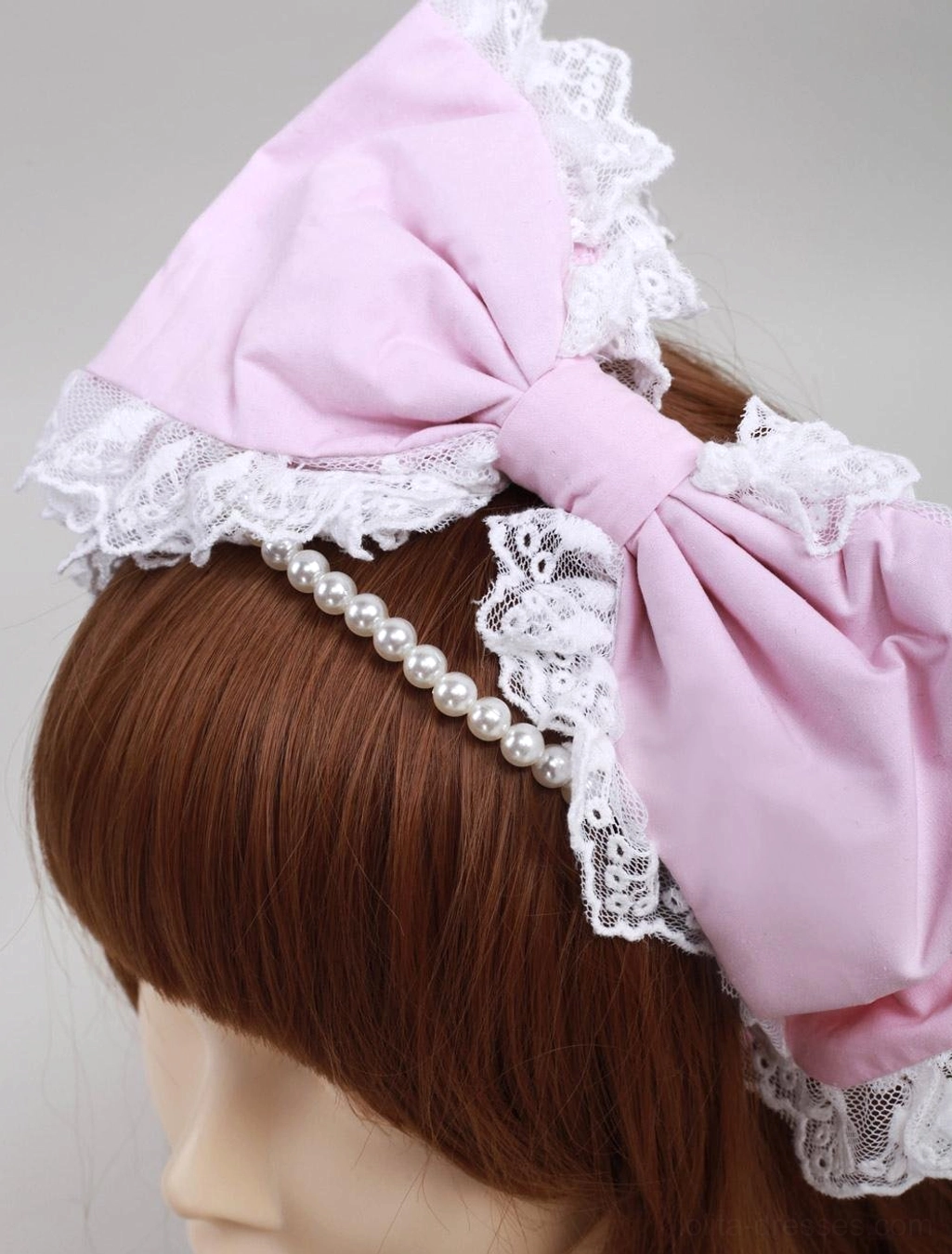 Pink lace pearl lolita headdress with white ruffled trim and faux pearl chain, side close-up view on mannequin with brown hair, showing intricate lace details and pearl embellishments