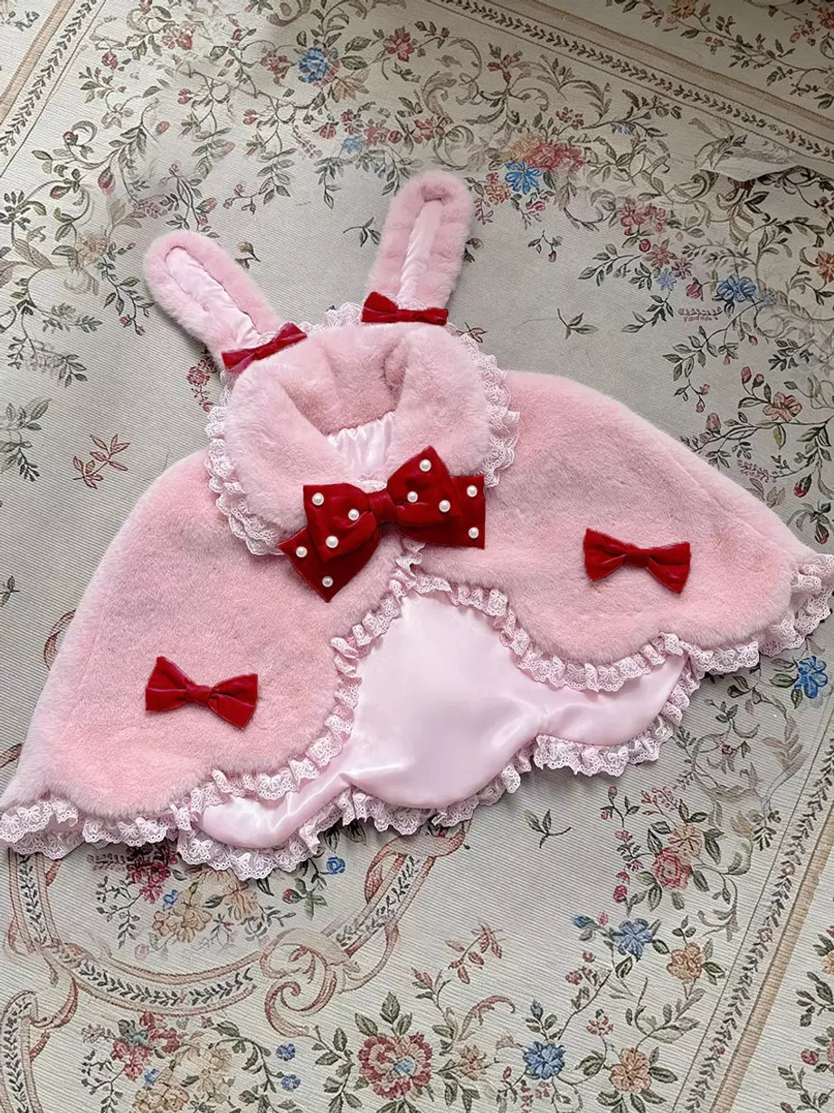 Pink plush lolita bunny ear cape with red polka-dot bow and coordinating side bow accents, flat lay display on vintage fabric