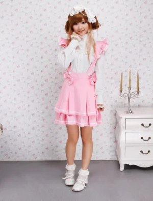 Pink polka dot tiered cotton lolita skirt full front view with ruffled shoulder straps, white trim details, and layered pleated skirt silhouette worn with white accessories and floral headwear