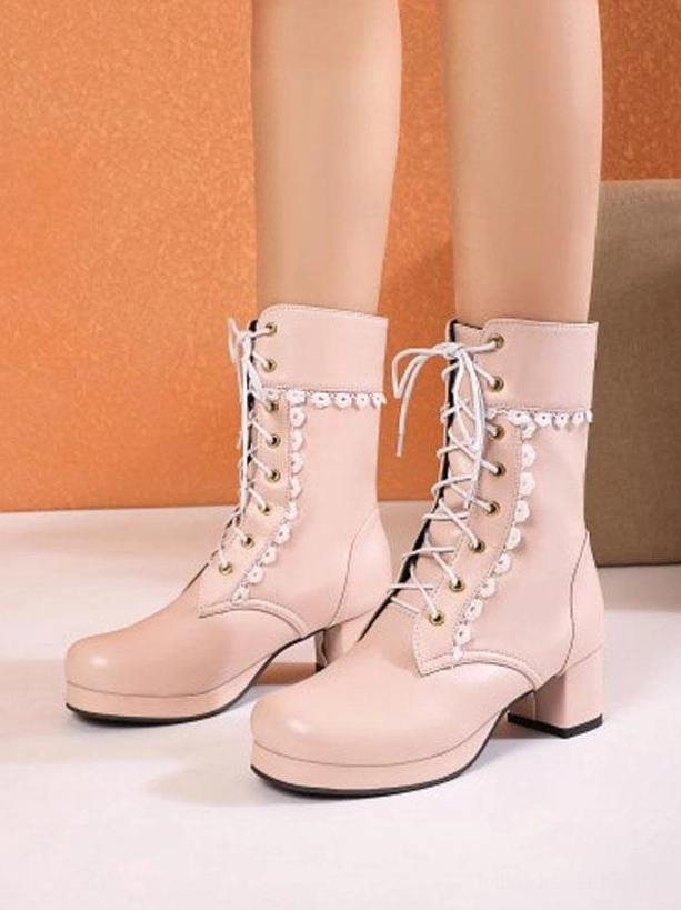 Pink lace-up Lolita ankle boots with round toe and chunky block heel featuring decorative white floral lace collar on orange wall background