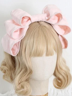 Pink oversized double-layered Rococo Lolita bow headband displayed on blonde wig mannequin, front flat view showing woven polyester texture and voluminous bow silhouette