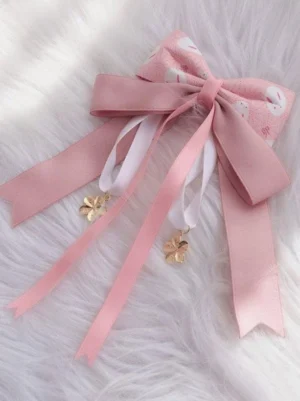 Pink sakura bow lolita hair clip with bunny print design featuring golden flower pendants and dual-color ribbons on white fuzzy background - front flat lay view