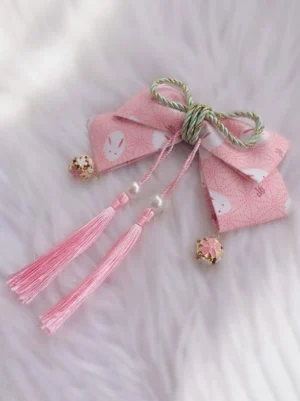 Pink sakura rabbit print lolita hair bow headdress with gold bell charms and pink tassel fringe on white fuzzy background flat lay