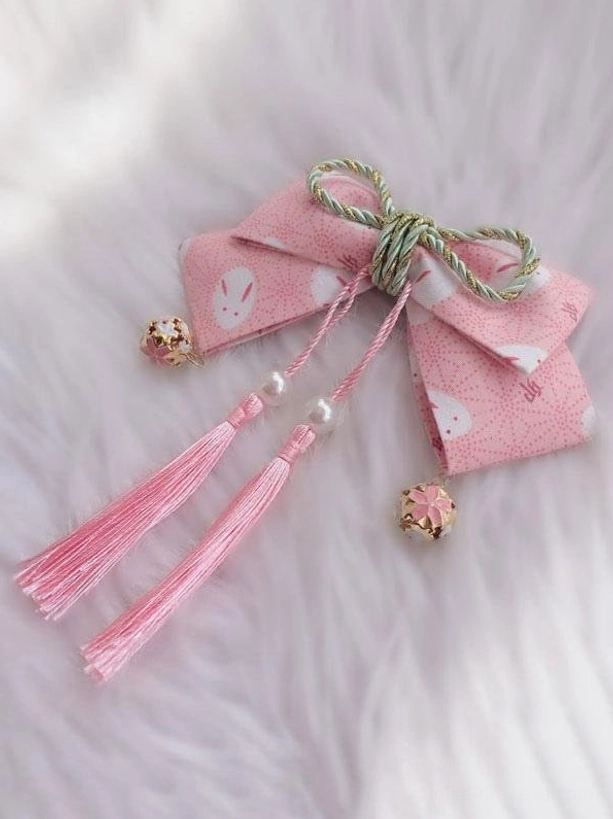 Pink sakura rabbit print lolita hair bow headdress with gold bell charms and pink tassel fringe on white fuzzy background flat lay