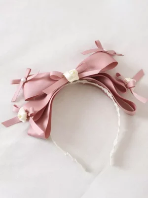 Overhead flat lay view of pink satin bow lolita headband showing white lace lined interior, delicate bow structure and pearl rose accent details arranged on soft white fabric background, showcasing headwear construction and romantic embellishment design