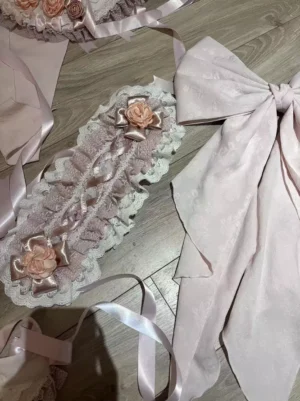 Pink sweet lolita accessories set featuring decorative lace headpieces with satin rose embellishments and oversized pink satin bows displayed on wooden desktop flat lay