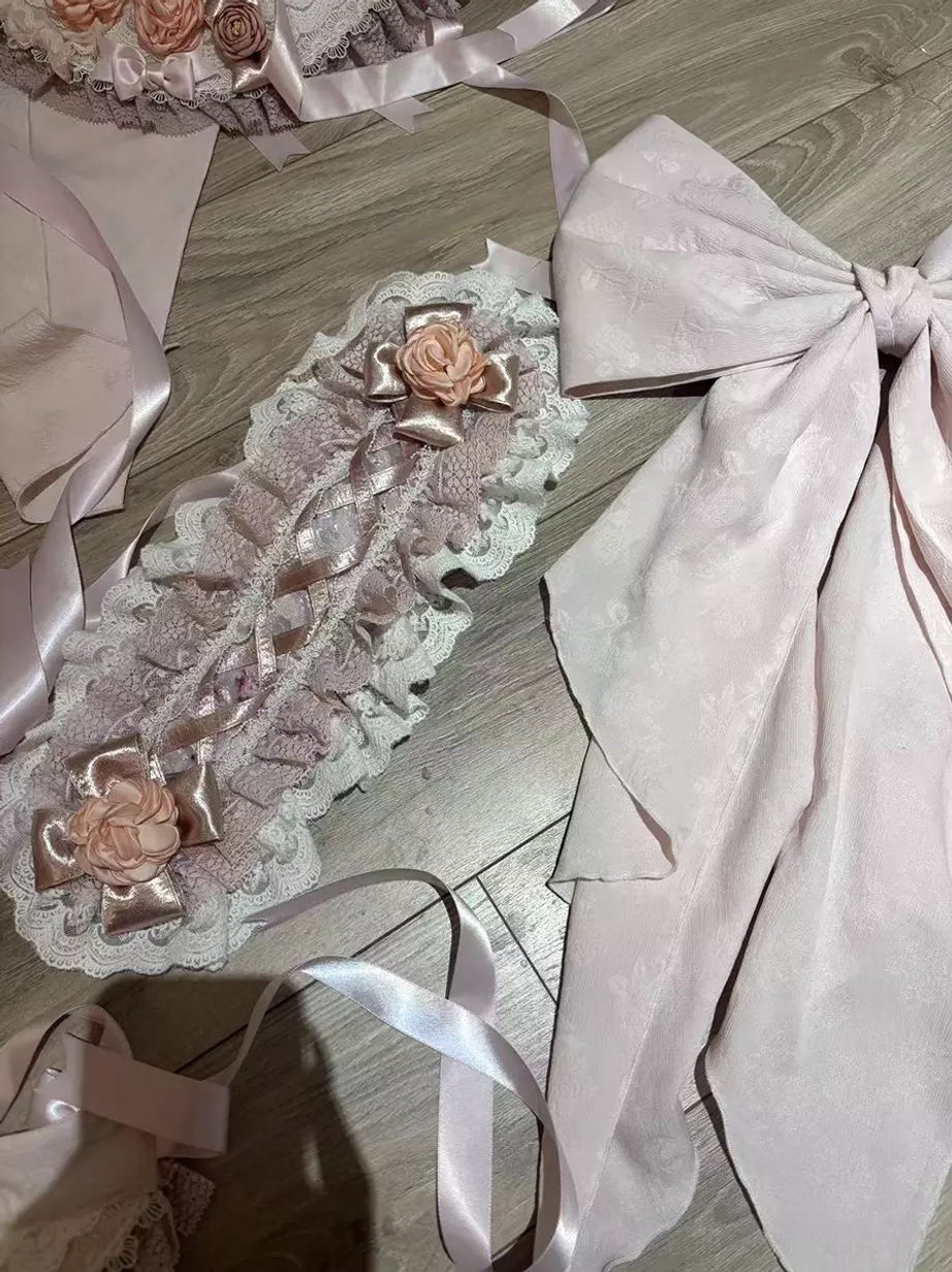 Pink sweet lolita accessories set featuring decorative lace headpieces with satin rose embellishments and oversized pink satin bows displayed on wooden desktop flat lay