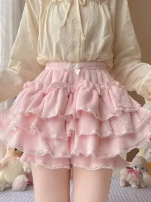 Pink sweet lolita bloomers with tiered ruffles and lace trim worn with beige ruffled blouse, front waist-down view showing fuzzy velvet texture and small bow detail