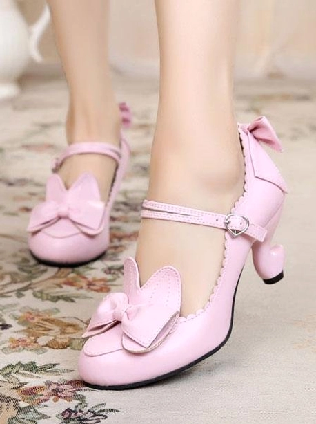 Soft pink lolita heels with bow details and cat-ear embellishment on floral carpet, side close-up of worn feet showing quintessential sweet lolita style
