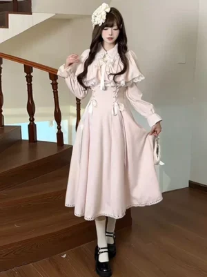 Pink sweet lolita dress with false two-layer cape overlay and long sleeves worn by model on wooden staircase full body front view