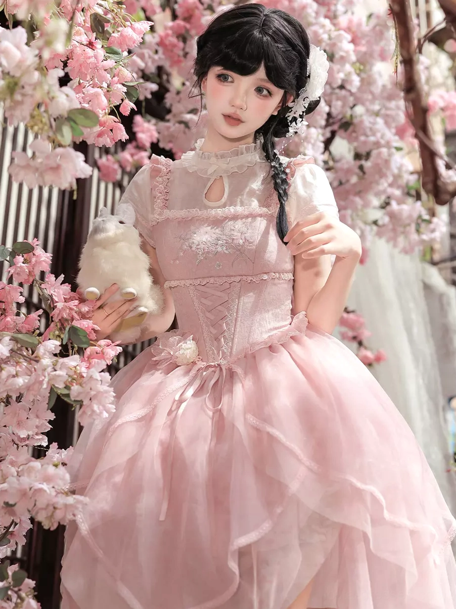 Close-up front view of pink sweet lolita midi dress showing floral lace bodice, waist satin bow accent, and sheer inner sleeves with model holding plush rabbit