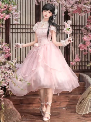 Full body front view of pink sweet lolita dress featuring short puff sleeves, lace-up corset top, and voluminous tulle skirt worn on terrace with cherry blossoms
