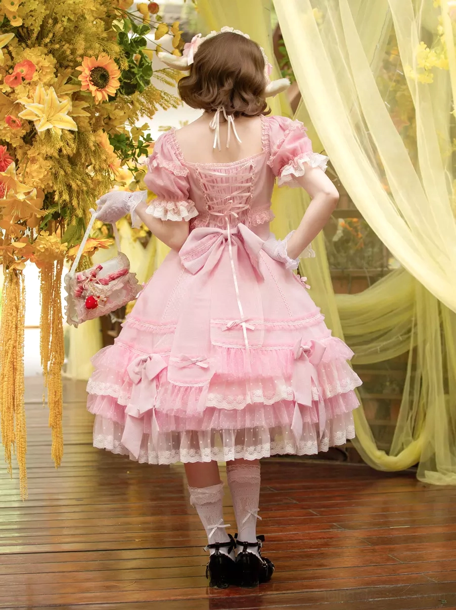 Pink sweet Lolita dress full rear view displaying large back bow tiered lace hem white stockings and shoes