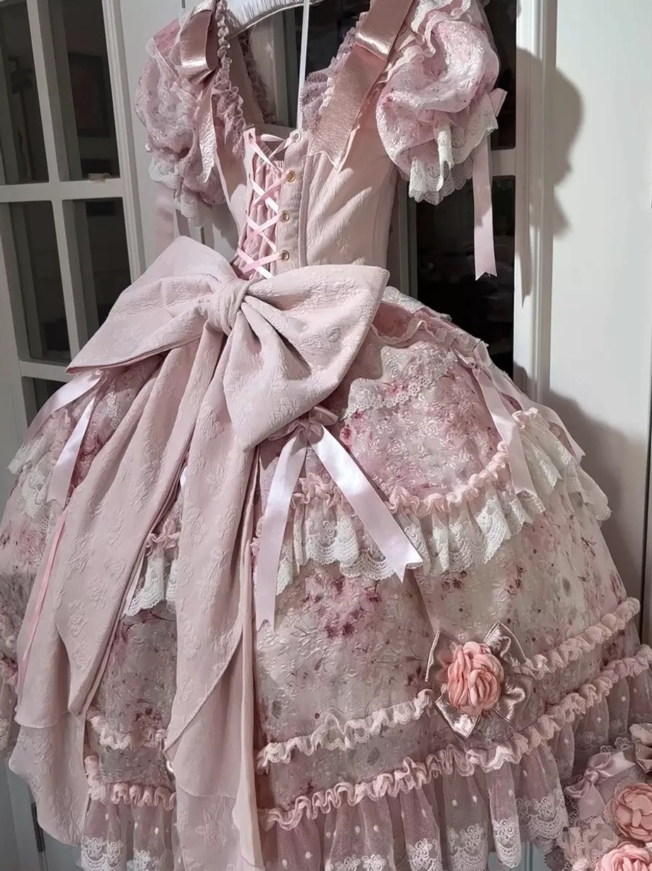 Pink sweet lolita formal gown side three-quarter view displaying V-neck lace-up bodice construction, ruffled short sleeves, and large oversized satin bow back detail
