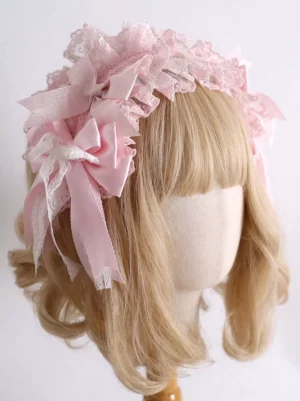 Pink sweet lolita headdress with ruffled lace crown and satin bows worn on mannequin with blonde wig, three-quarter left view showing layered lace design and delicate bow details