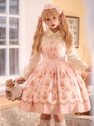 Pink sleeveless Sweet Lolita jumper skirt with vintage floral print and chest bow, front full view on model with blonde twin tails in cozy home setting