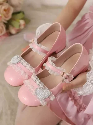 Pink sweet lolita mary jane pumps with ruffled ankle strap and heart rhinestone buckle, patent leather finish, held in hand over pink lolita dress and flower props, close-up overhead view