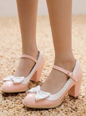 Pink sweet lolita mary jane pumps with white bow and scalloped trim worn on-foot front view on gravel ground showing ankle buckle strap detail