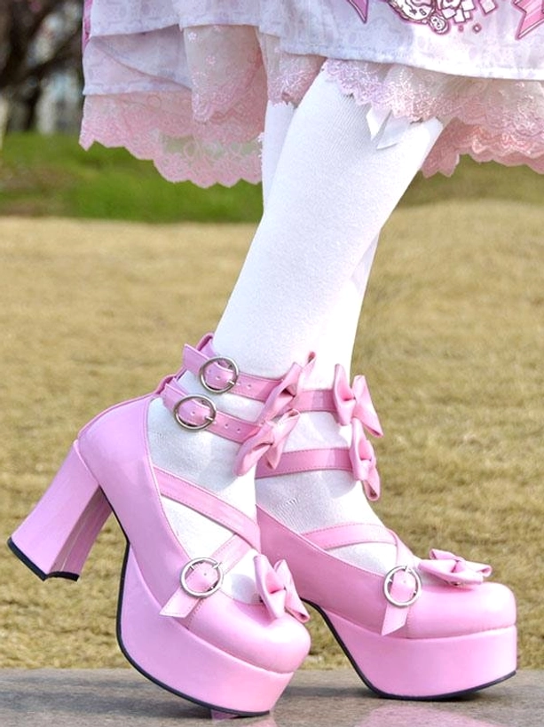 Pink Sweet Lolita platform pumps with pink patent leather bow details and chunky heel, worn with white stockings on outdoor grass, side close-up view showing ankle strap buckles and round toe