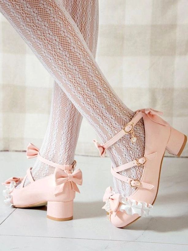 Pink sweet lolita chunky heel pumps with back bow embellishment and ruffle trim shown from rear side angle of model's legs wearing fishnet lace socks, highlighting ankle buckle strap and feminine silhouette