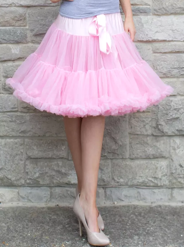 Pink tulle lolita underskirt petticoat full-body standing view on female model outdoor stone wall showing knee-length poof silhouette front satin bow