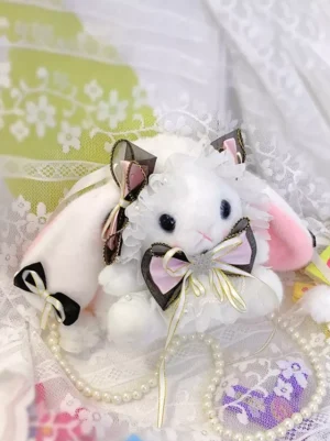 Plush rabbit lolita crossbody bag with bunny pattern, black bows and pearl details, flat lay top-down view on white and pink lace background, sweet rococo style