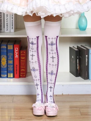 Rear full view of model wearing white over-the-knee lolita socks with purple cross lace prints, paired with pink frilly skirt and pink bow flats, styled in cozy bookshelf setting with wooden floor