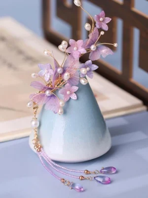 Purple sheer organza flower lolita hair ornament with gold branches pearl accents and cascading purple crystal tassel displayed on blue ceramic vase showing three-dimensional floral design and delicate craftsmanship