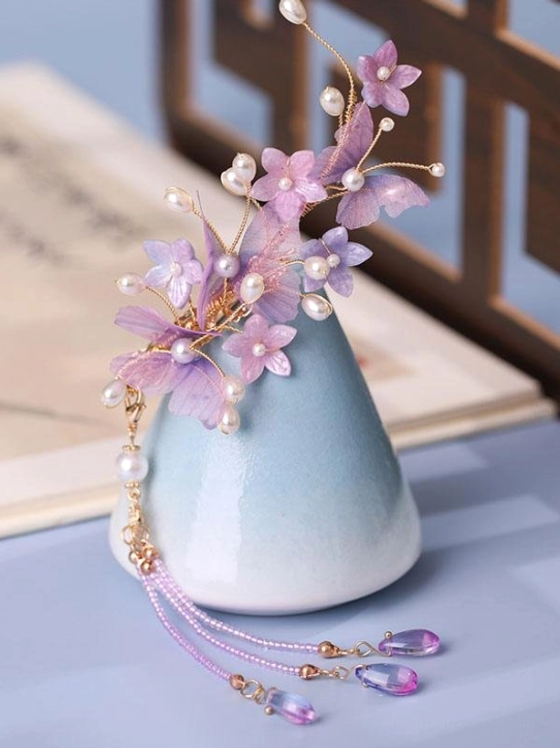 Purple sheer organza flower lolita hair ornament with gold branches pearl accents and cascading purple crystal tassel displayed on blue ceramic vase showing three-dimensional floral design and delicate craftsmanship