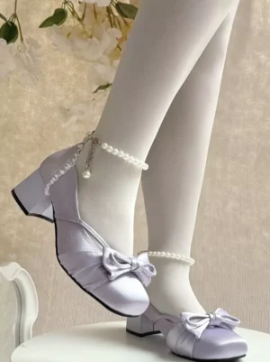 Purple satin lolita block heel pumps with bow ornament displayed on model leg wearing white tights and pearl ankle jewelry in oblique angle