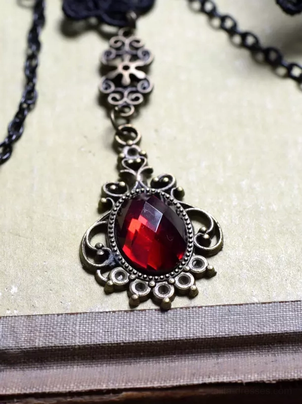 Red faceted gemstone pendant closeup with ornate brass-tone frame and hanging chain from gothic lolita arm cuff jewelry piece
