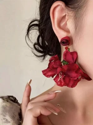 Red layered fabric flower drop earrings with green bead details worn on left ear model with french nails patterned clothing neck area fashion styling gothic lolita accessory jewelry