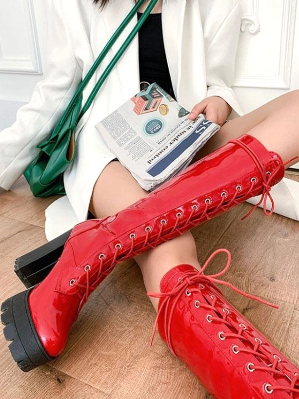 Red patent leather mid-calf boots overhead close-up with red laces visible, showing round toe and thick platform sole detail on wooden floor