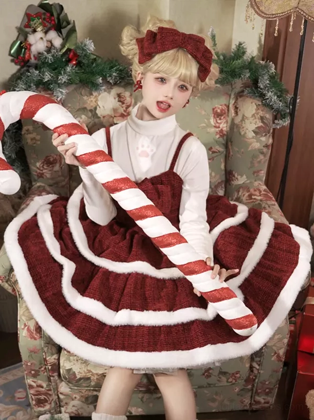 Dynamic front shot of red lolita Christmas slip dress set model holding giant candy cane prop with red-white striped decor on floral sofa