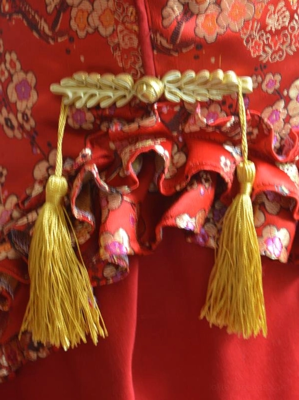 Waist decoration and ruffled trim detail of red lolita dress showing golden tassel pendants and brocade ruffled trim on satin base