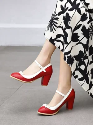 Red Mary Jane lolita pumps with round toe and ankle strap displayed on foot, paired with black floral print skirt, showing side view of chunky block heel and bow decoration