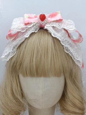 Rococo style Lolita bow headdress front view pink cameo color with strawberry embellishments and white lace frills on golden curly wig mannequin