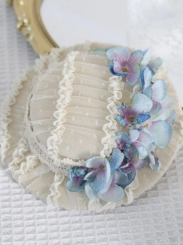 Overhead flat lay of beige pleated mesh Lolita mini hat with blue gradient hydrangea flowers and delicate ruffled lace trim detail