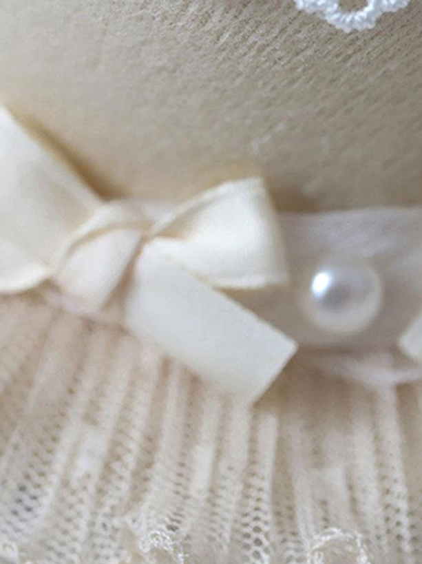 Close-up flat lay detail of rococo lolita hat cream satin bow faux pearl and ruffled lace texture