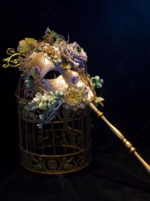 ornate masquerade handheld mask with purple blooms golden filigree and long golden rod on vintage metal birdcage