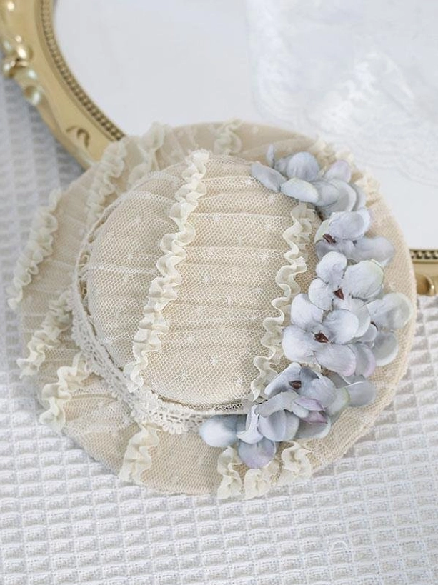 Overhead flat lay of off-white pleated mesh Rococo Lolita mini hat with light gray-blue hydrangea flowers and delicate ruffled lace edges